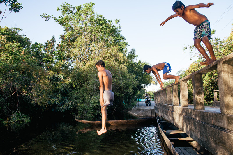 Photo Two indigenous Curripaco girls gossip in the kitchen, and boys jump off a road bridge into the river in the jungle town of Puerto Inírida, Guainia, 2010. 