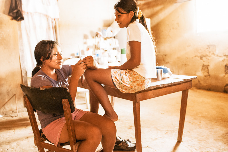 Photo Two indigenous Curripaco girls gossip in the kitchen, and boys jump off a road bridge into the river in the jungle town of Puerto Inírida, Guainia, 2010. 